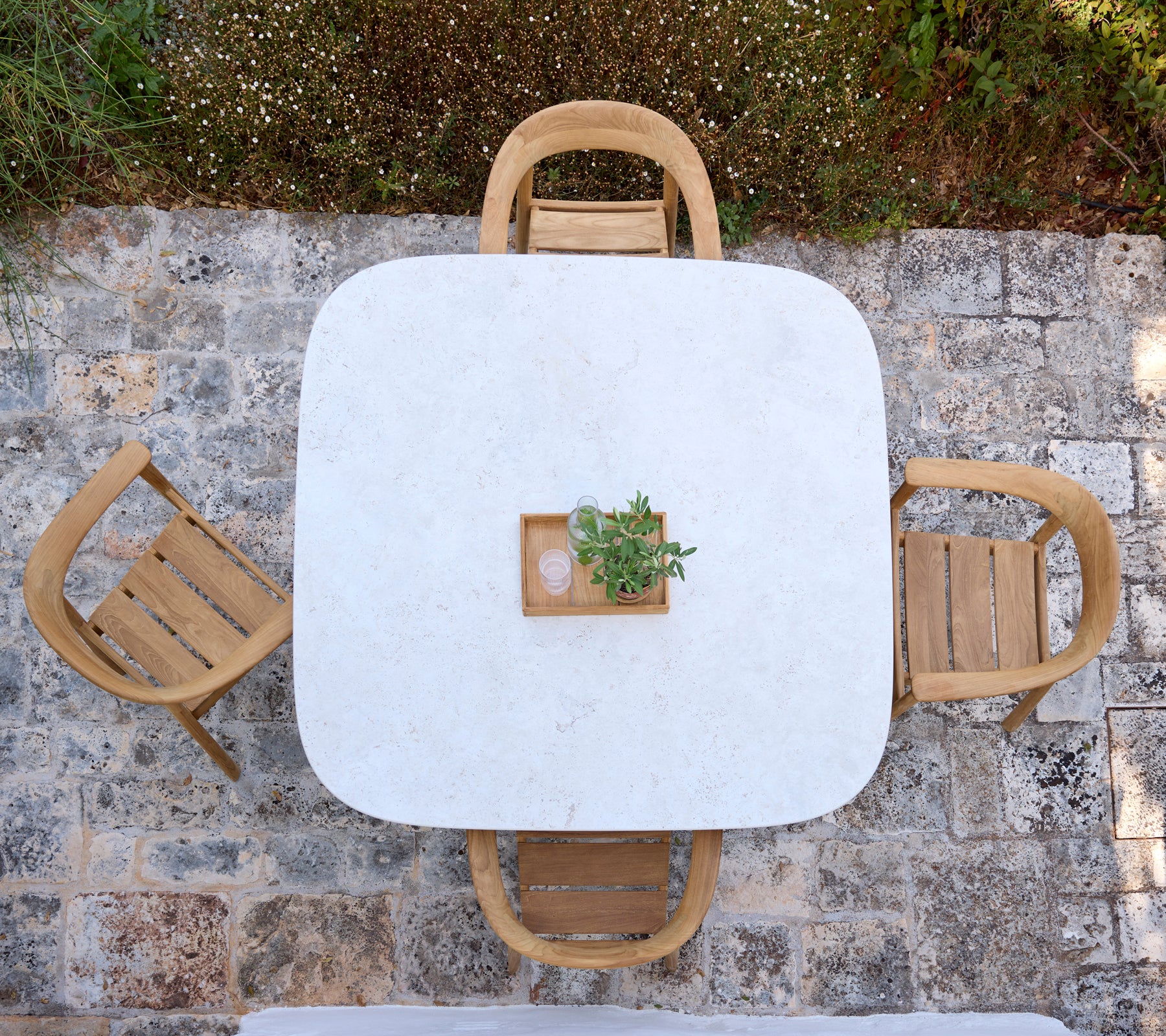 Moderner weißer Tisch mit Holzstühlen und einem kleinen Pflanzen-Centerpiece in einem Außenbereich.
