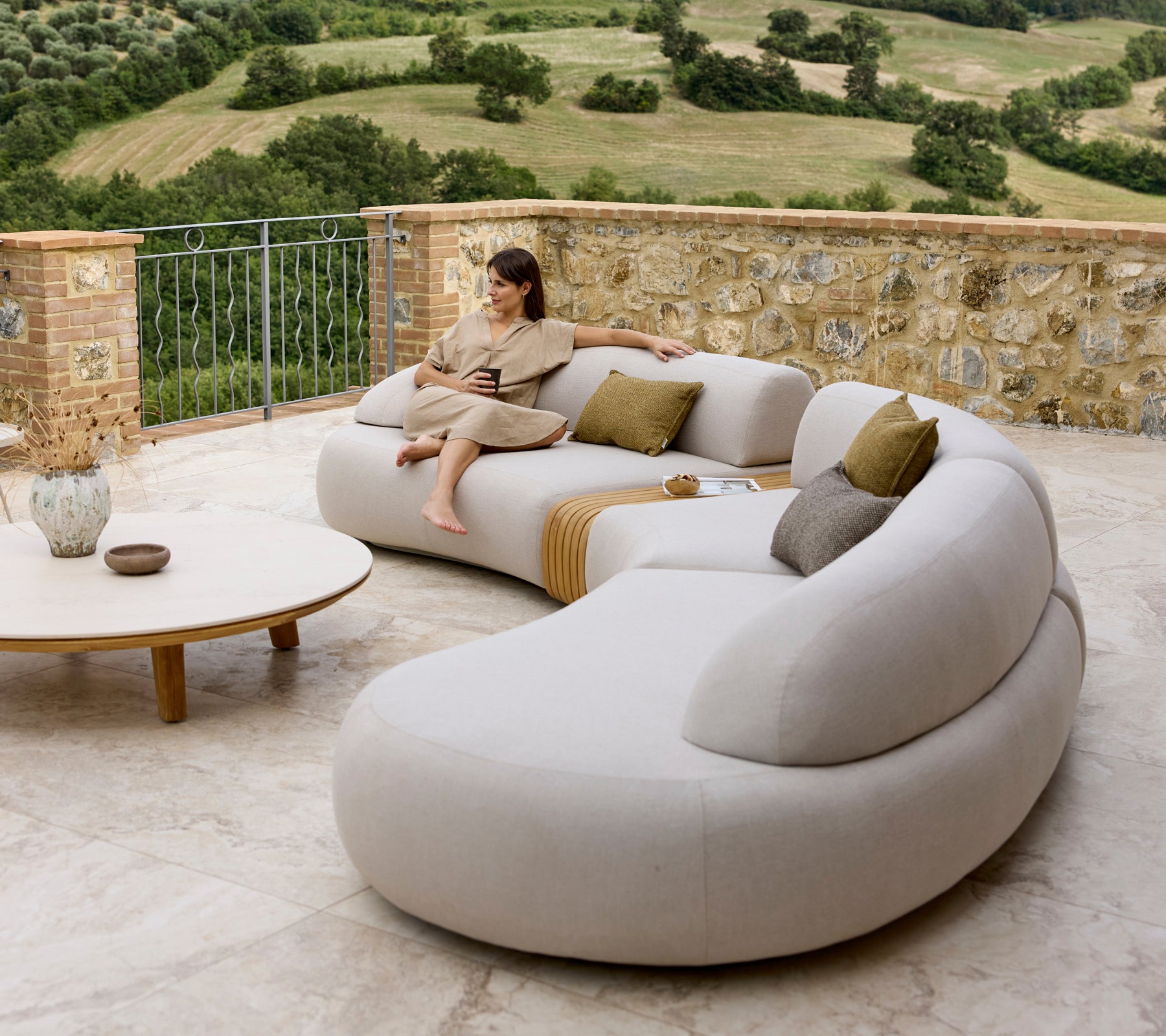 Ein stilvolles Lounge-Sofa mit sanften Kurven und Kissen, ergänzt durch einen runden Couchtisch, mit einem malerischen Ausblick.