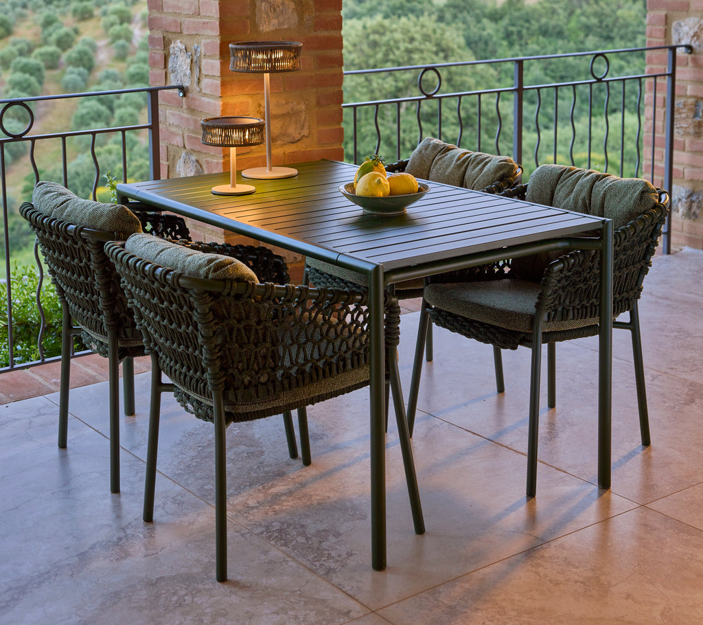 Ein stilvoller grüner Ocean-Esszimmerstuhl um einen rechteckigen Tisch, ergänzt durch eine dekorative Lampe und eine Schüssel mit Obst.