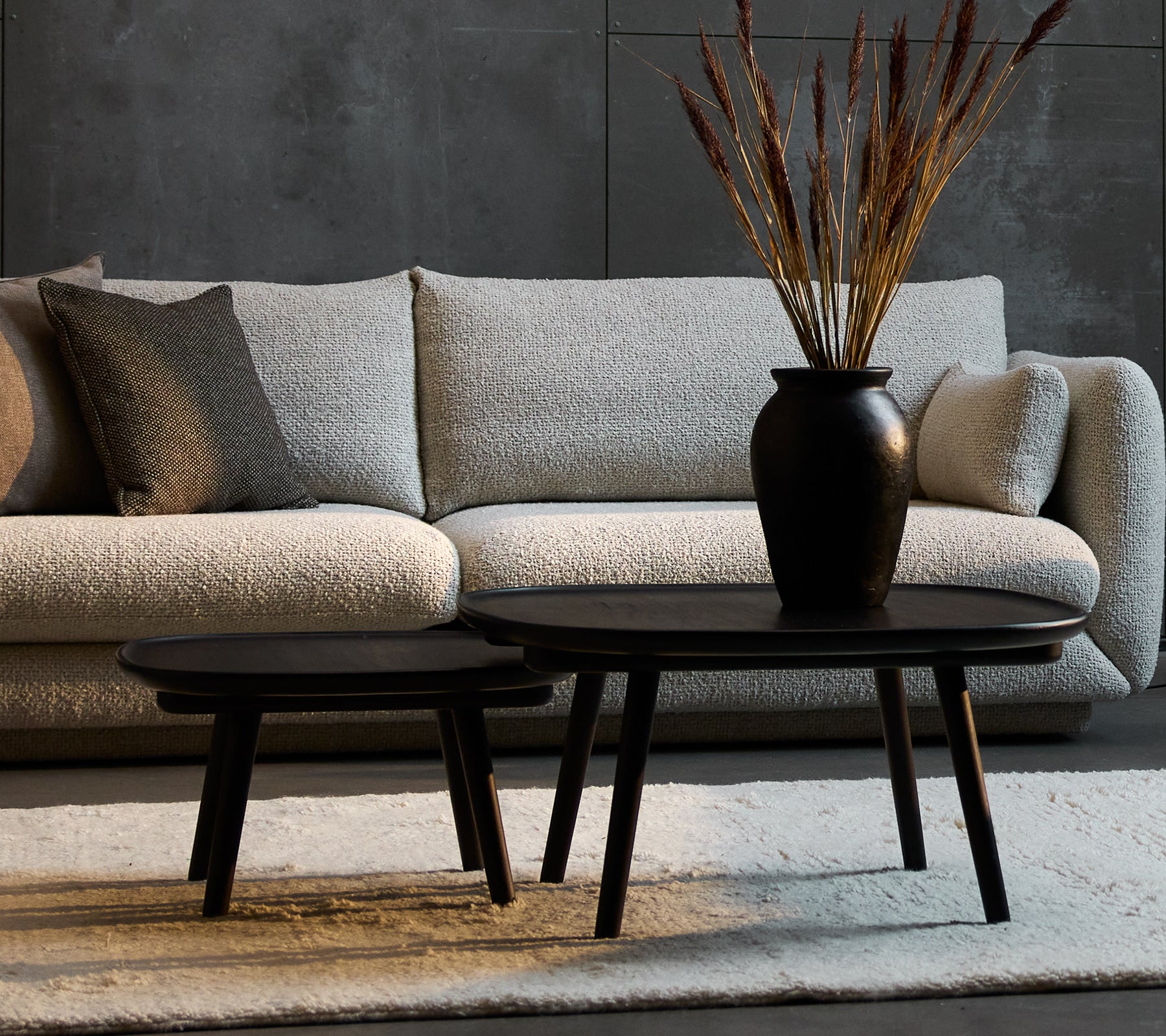 Zwei elegante schwarze Couchtische in verschiedenen Größen, ergänzt durch eine dekorative Vase mit getrockneten Pflanzen, vor einem gemütlichen Sofa.