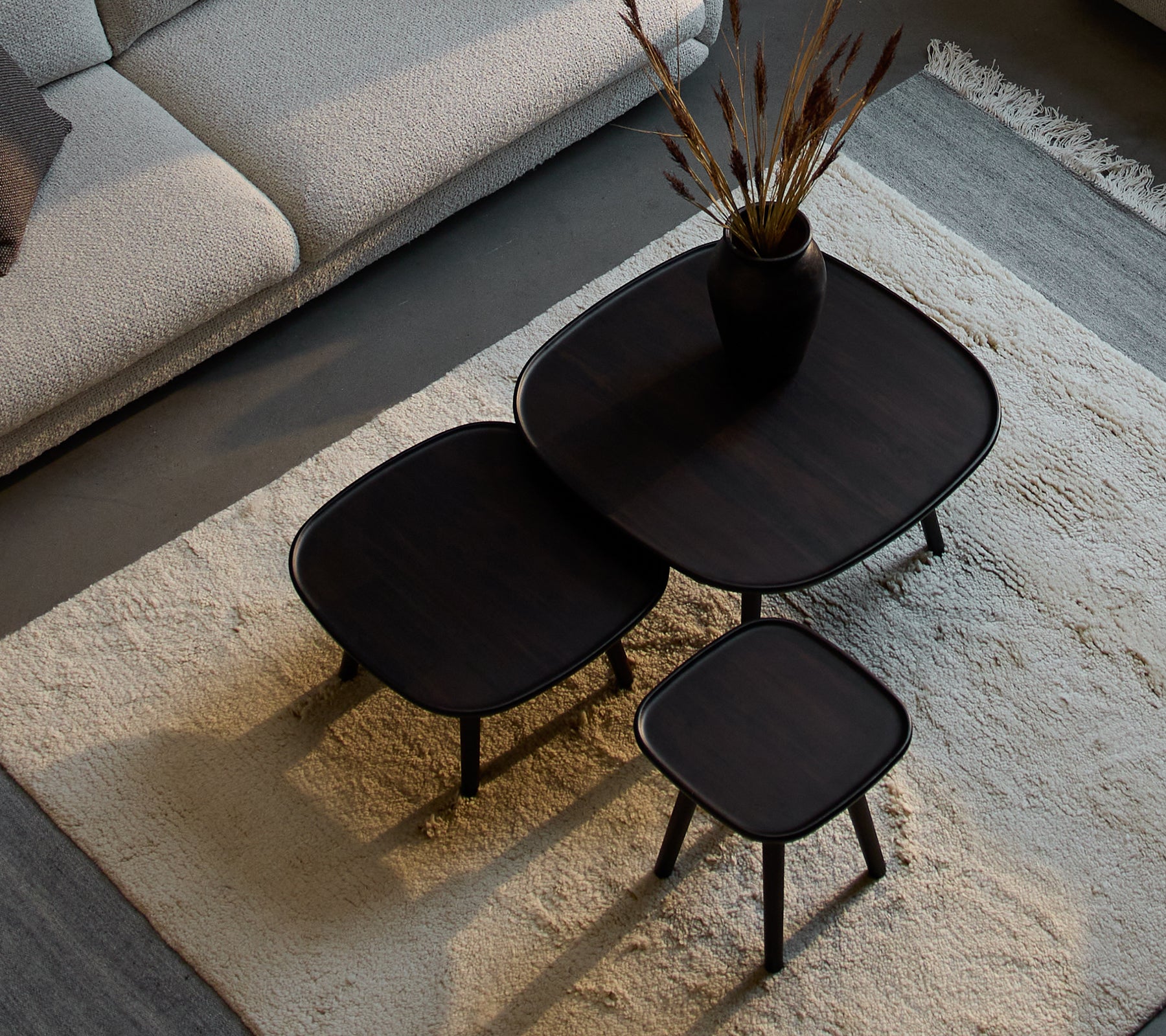 Drei stilvolle Pace- couchtische in verschiedenen Größen, mit einem eleganten Design und dunkler Oberfläche, begleitet von einer dekorativen Vase und Trockenpflanzen.