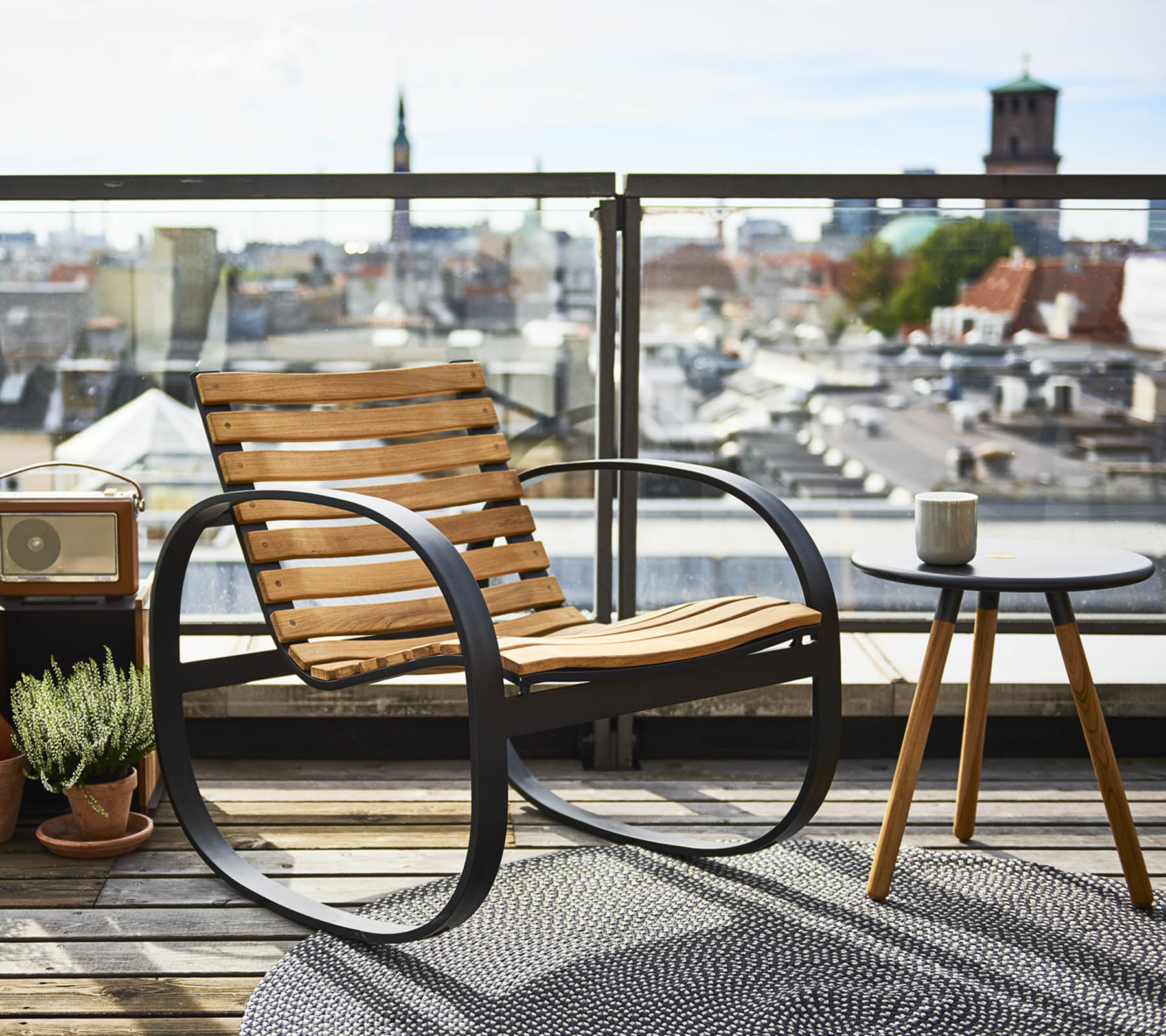 Ein stilvoller Schaukelstuhl neben einem kleinen Beistelltisch mit Blick auf eine panoramische Stadtansicht, geschmückt mit einer Pflanze und einem Teppich.