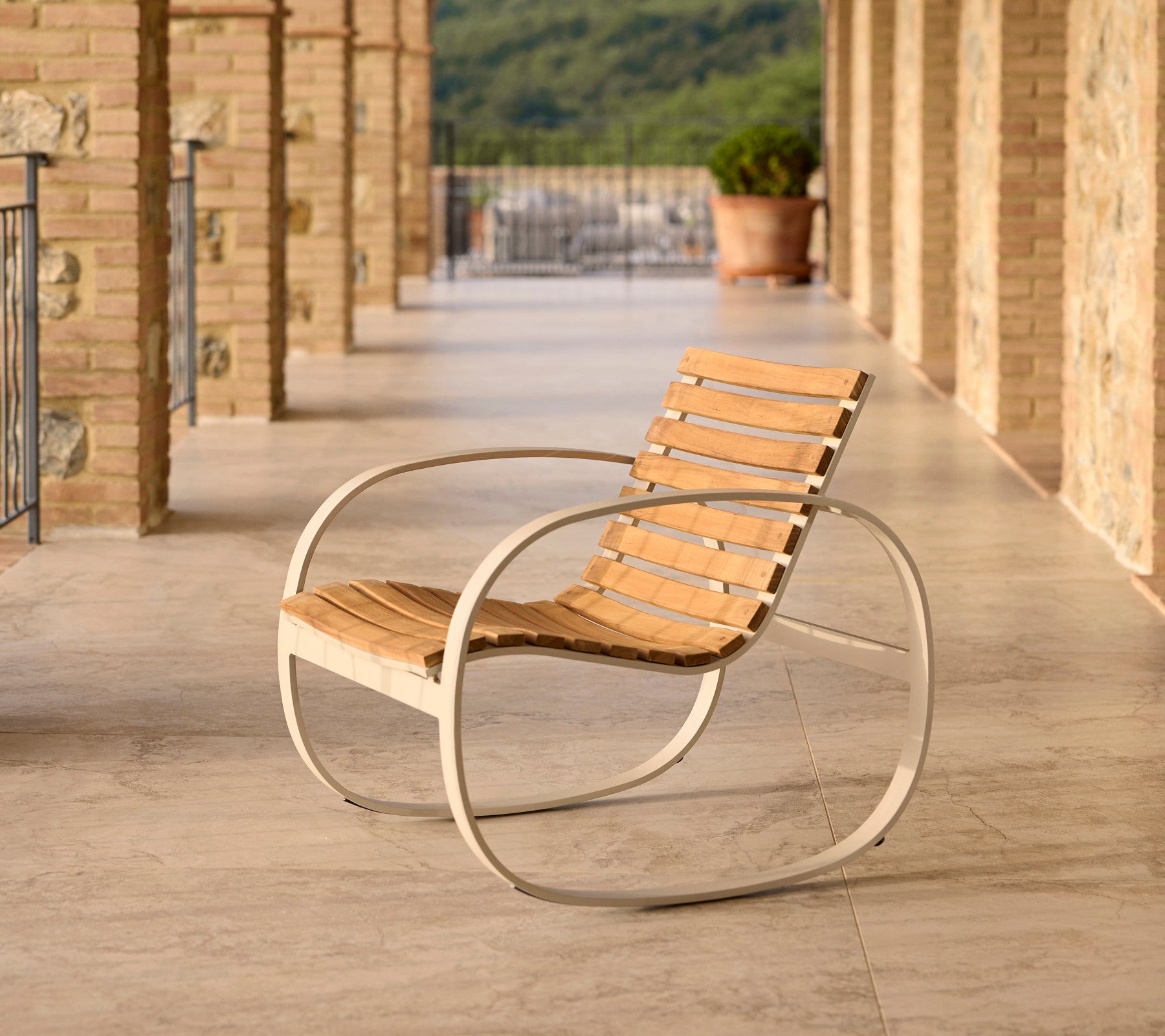 Parc Schaukelstuhl mit einem Aluminiumrahmen und Holzlatten, platziert auf einer Terrasse mit Steinboden und malerischer Kulisse.