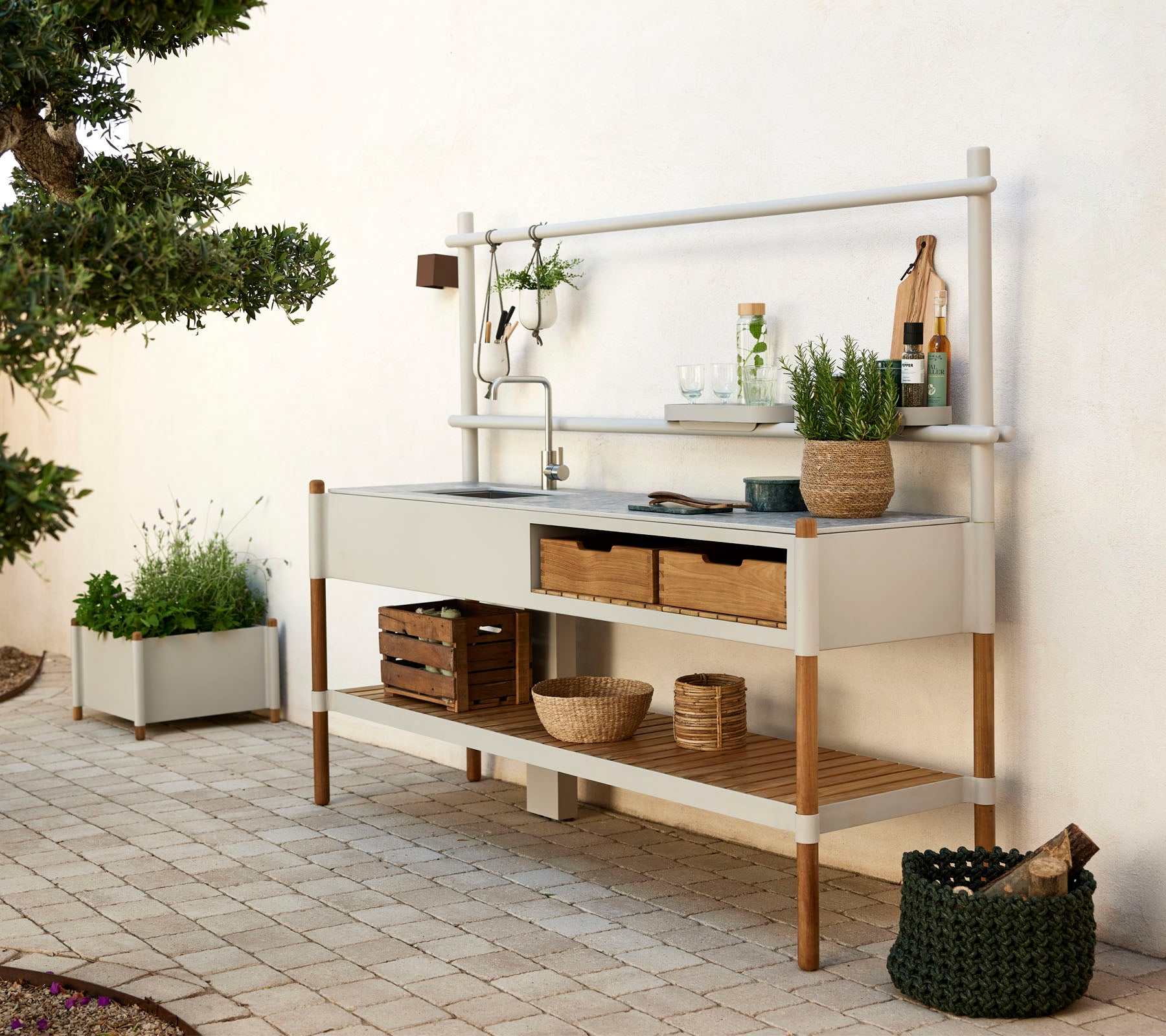 Moderne Küchenmöbel mit einem Metallbecken, Holzregalen und dekorativen Pflanzen in stylischen Behältern. Sauberes Design mit natürlichen Elementen.