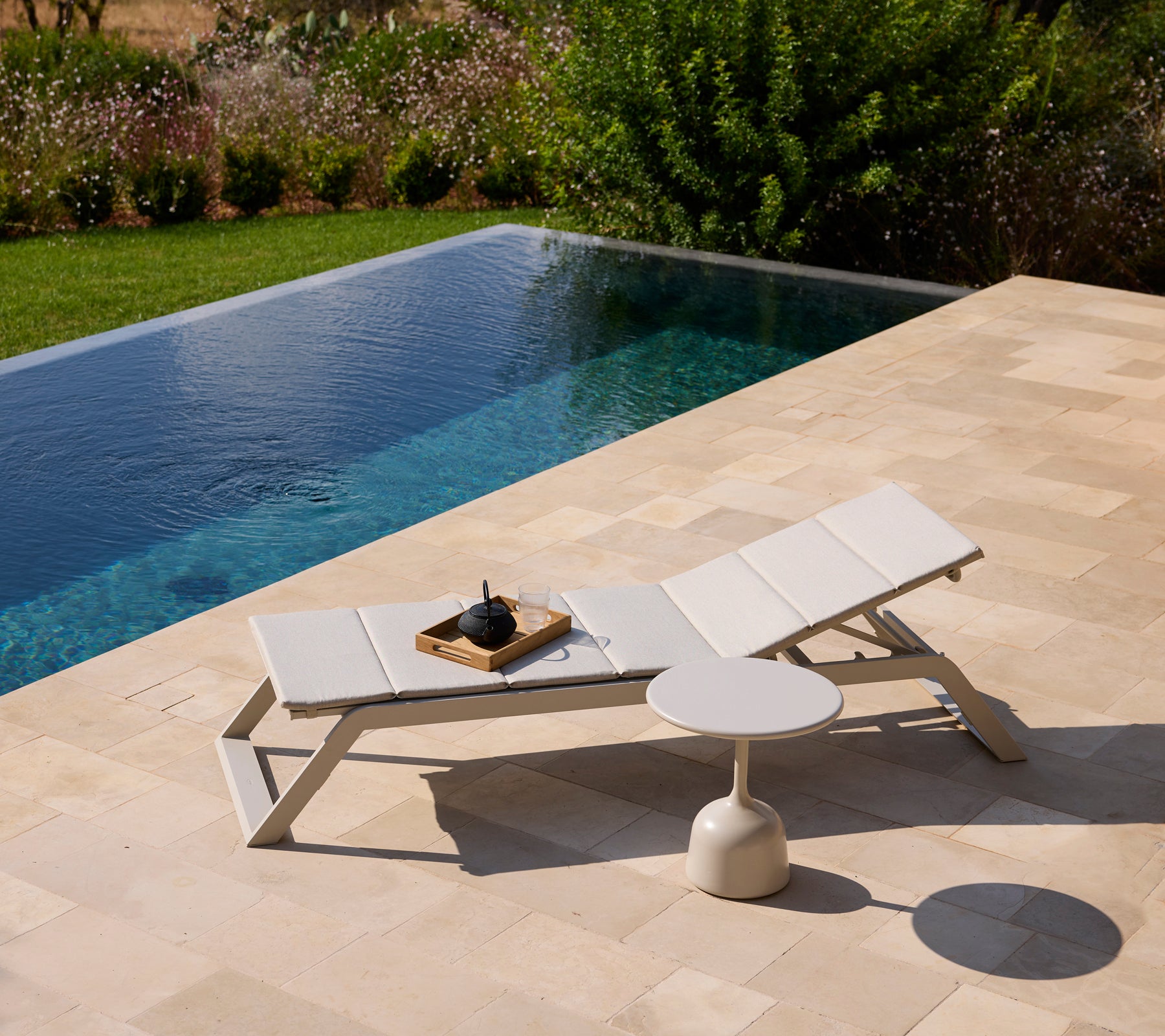 Moderner weißer Loungestuhl und Beistelltisch an einem Pool, umgeben von Grünflächen.