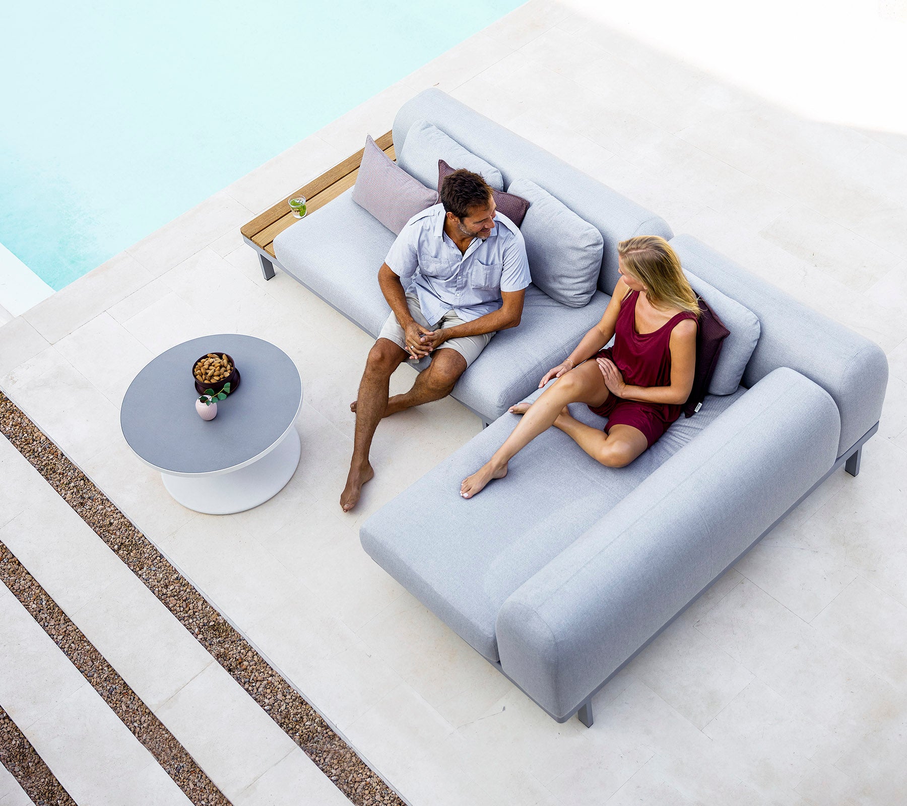 Ein Mann und eine Frau sitzen auf einem modernen grauen Sofa und führen ein Gespräch, mit einem kleinen Tisch und dekorativen Gegenständen in der Nähe.