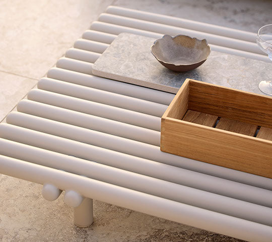 Aluminiumkaffee-tisch mit Lamellen-Design, ausgestattet mit einer Holzaufbewahrungsbox und einer Keramikschüssel auf einer minimalistischen Oberfläche.