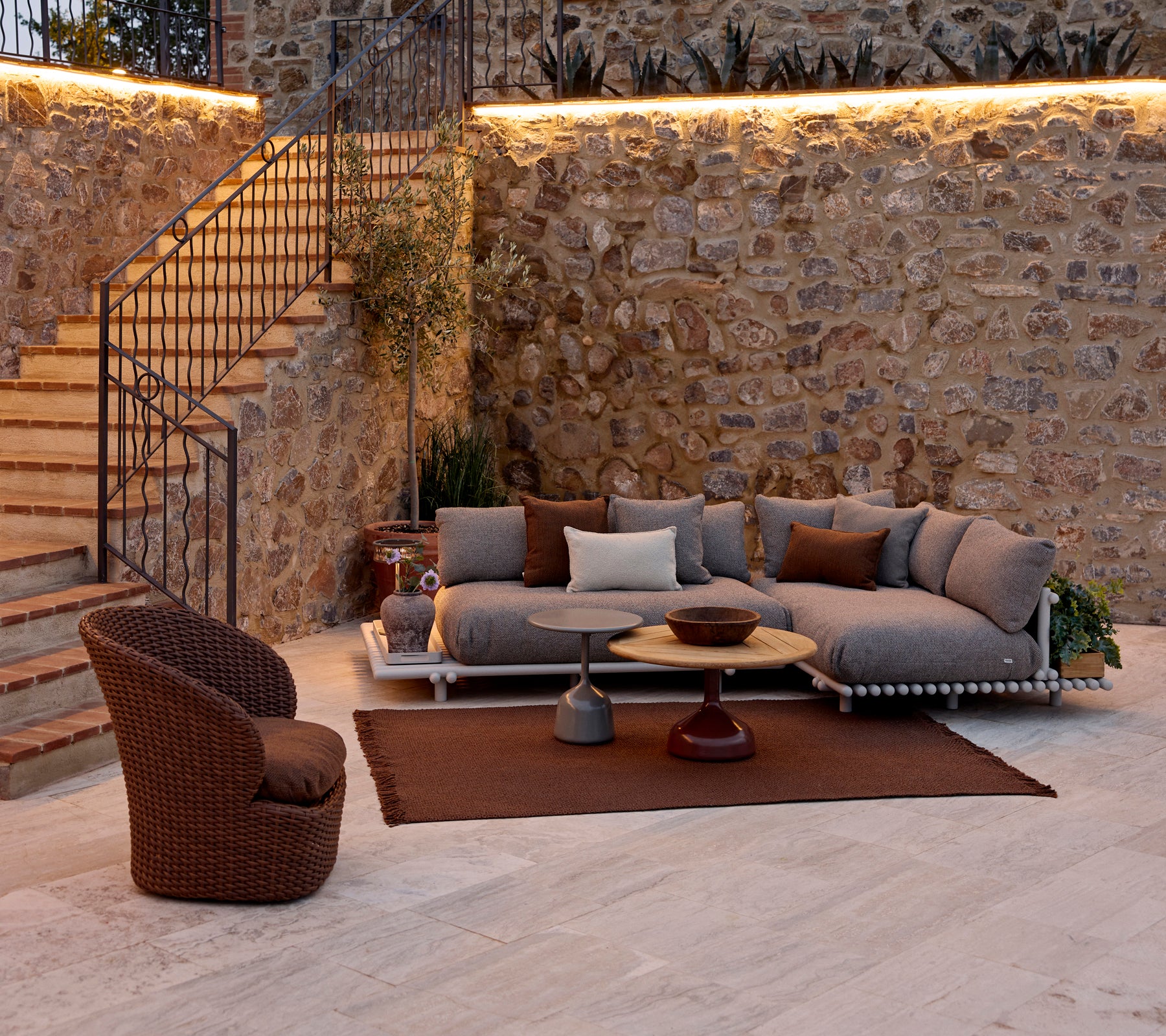 Gemütlicher Sitzbereich mit einem modularen Sofa mit Kissen, einem runden Couchtisch, einem gestrickten Teppich und einem geflochtenen Loungesessel.