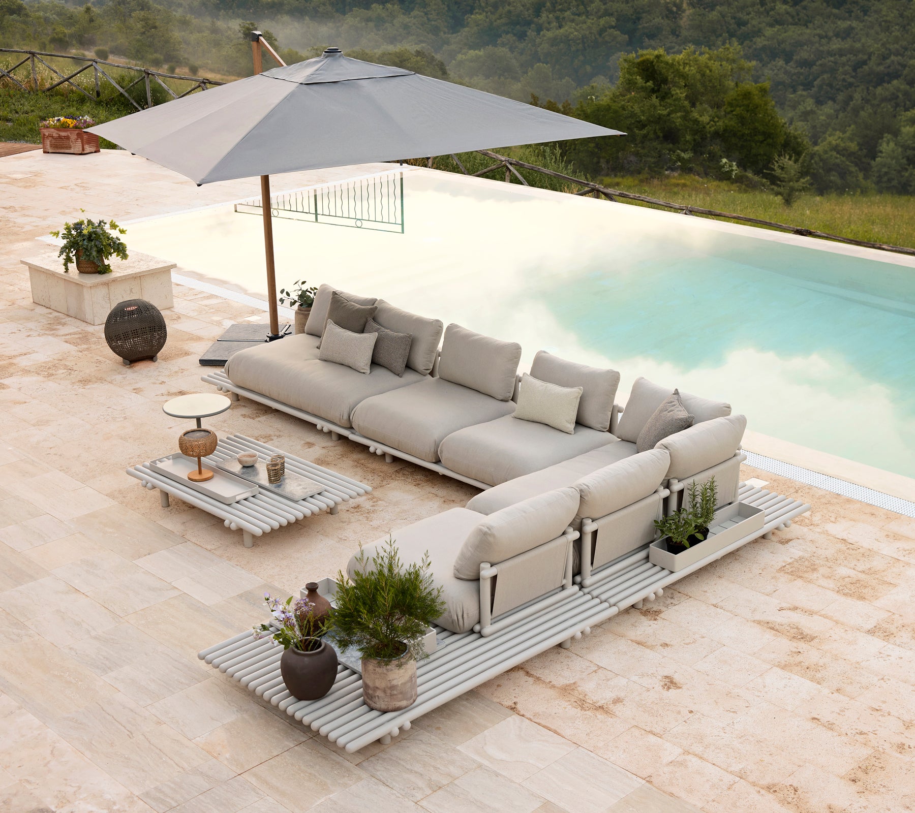 Stylisches Aluminium-Loungebereich mit plüschigen Kissen und einem passenden Couchtisch, ergänzt durch einen Sonnenschirm und dekorative Pflanzen.