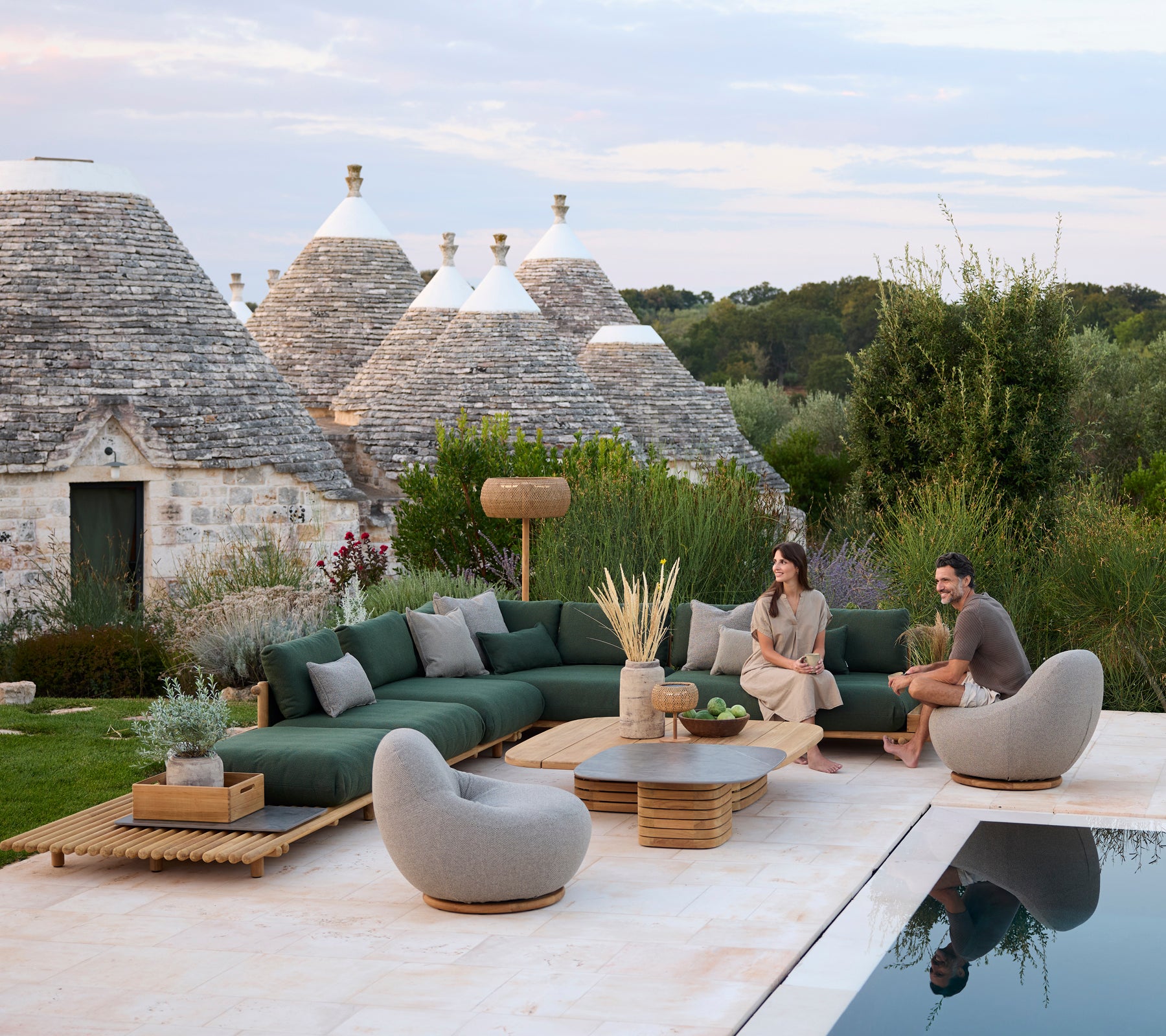 Moderne Außenlounge mit grüner Ecksofa und grauen Stühlen am Pool.