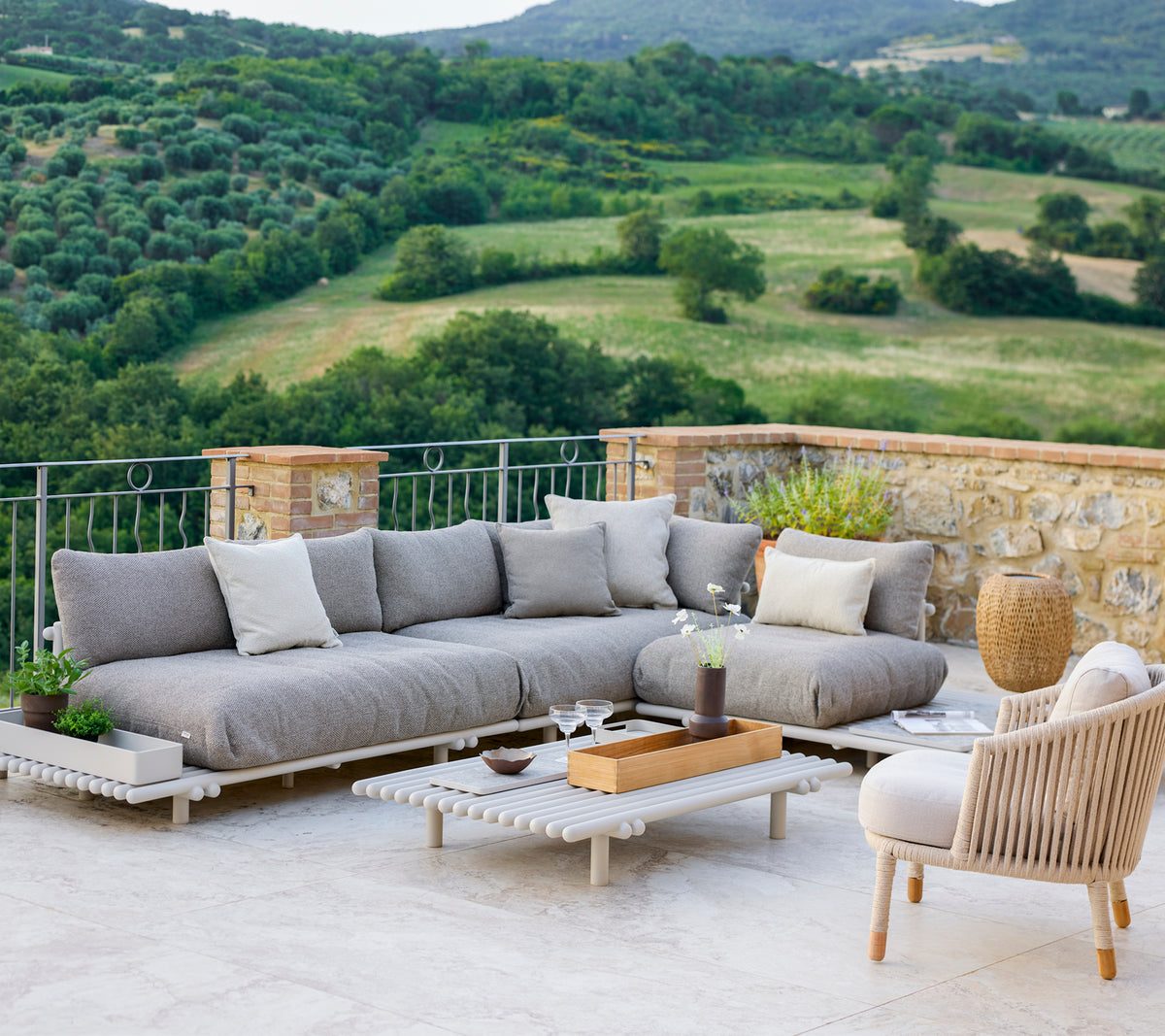 Stilvolles Lounge-Bereich mit einem grauen Ecksofa und einem bequemen Stuhl, vor einer malerischen Landschaft.