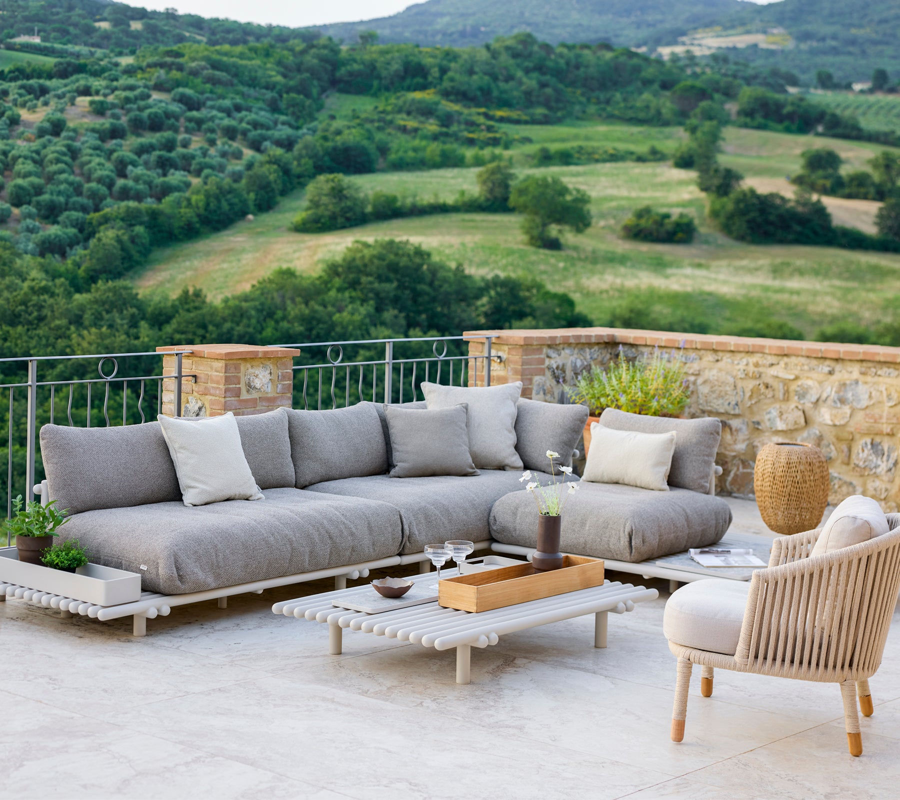 Stilvolles Lounge-Bereich mit einem grauen Ecksofa und einem bequemen Stuhl, vor einer malerischen Landschaft.