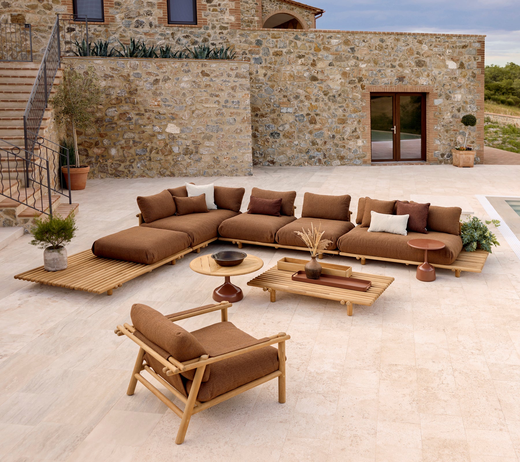 Ein stilvolles Lounge-Bereich mit einer Eckcouch mit plüschigen Kissen, einem Couchtisch und einem Teak-Lounge-Stuhl vor einer Steinwand.