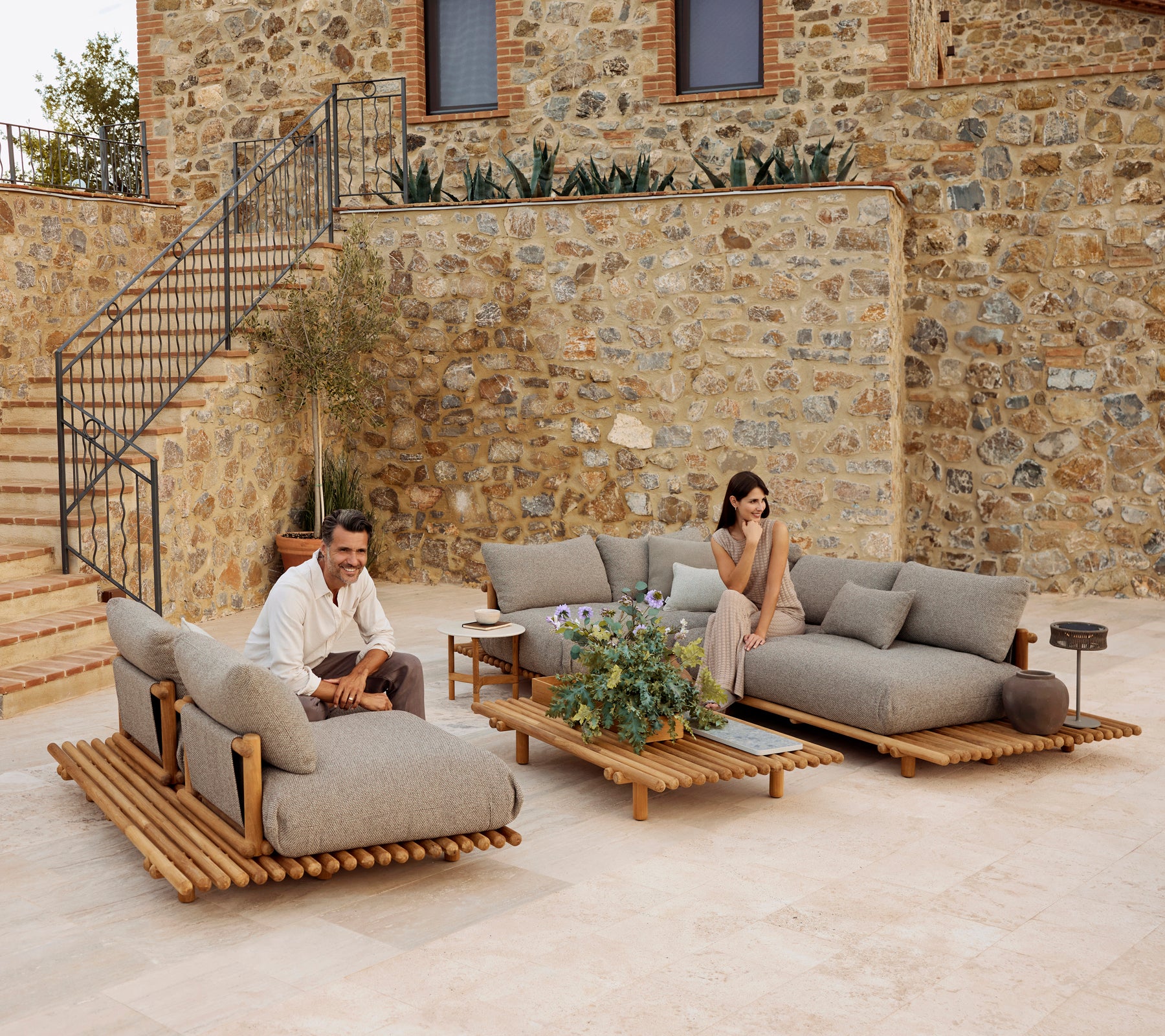 Ein stilvolles Lounge-Bereich mit Teakmöbeln, gepolsterten grauen Kissen, akzentuiert durch Grünpflanzen und einen modernen Couchtisch.