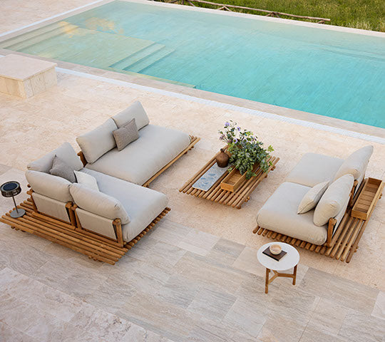 Stilvolle Teakmöbel mit Natte Kissen, ergänzt durch einen passenden Couchtisch und eine Topfpflanze, die neben einem ruhigen Pool steht.