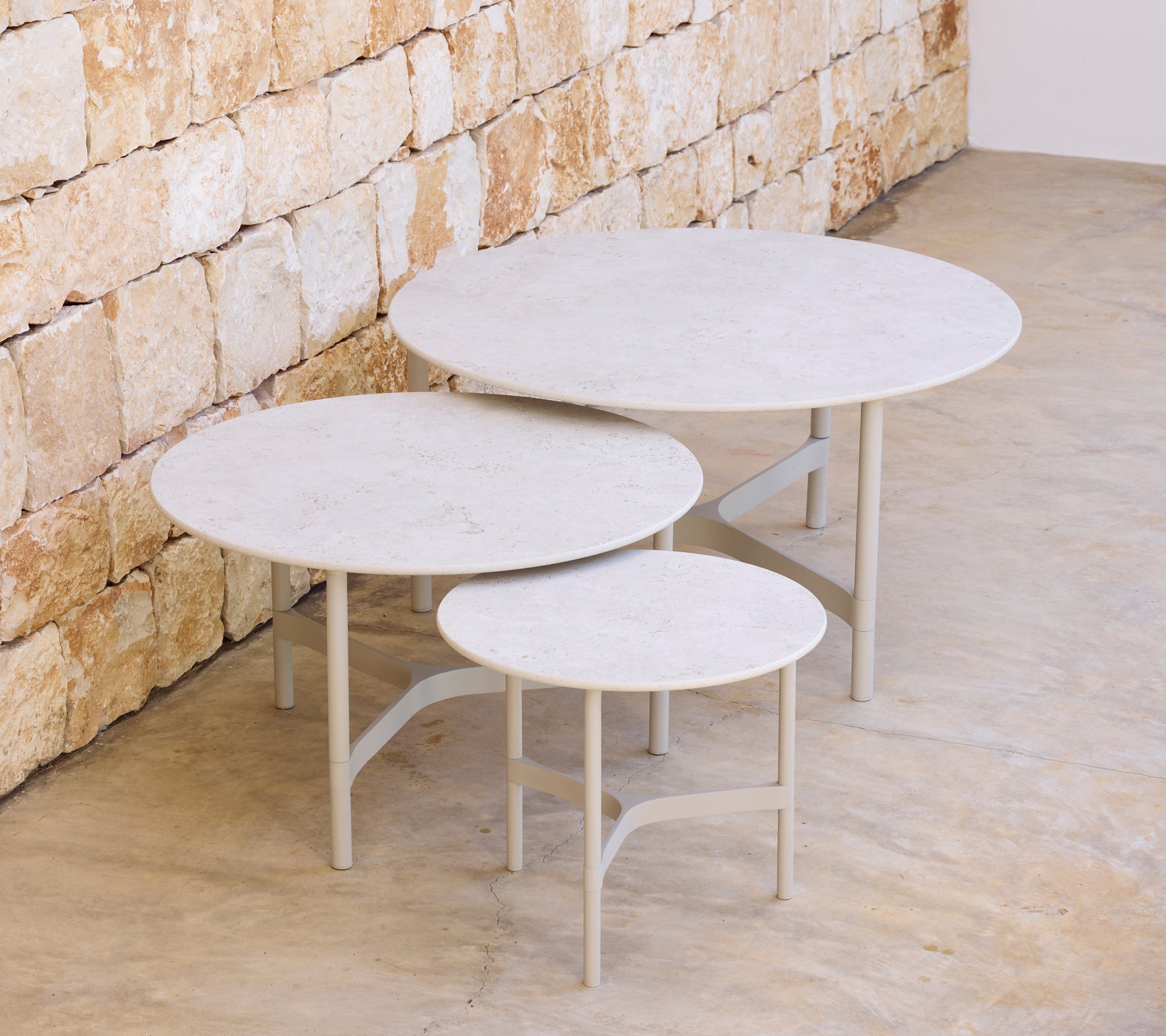 Drei moderne runde Tische in unterschiedlichen Größen gegen eine Steinwand.