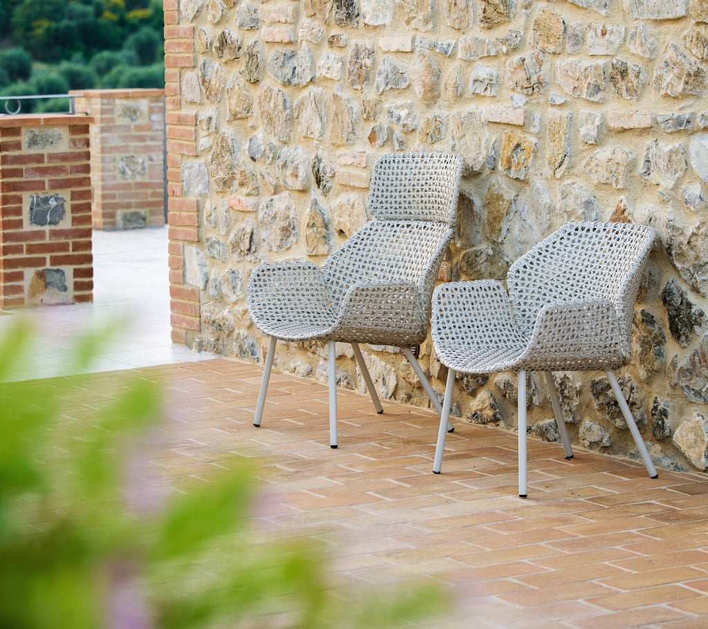 Zwei Vibe Hochlehner in dunklem Sand, stilvoll gestaltet, vor einer strukturierten Steinwand, die eine warme, einladende Atmosphäre schafft.