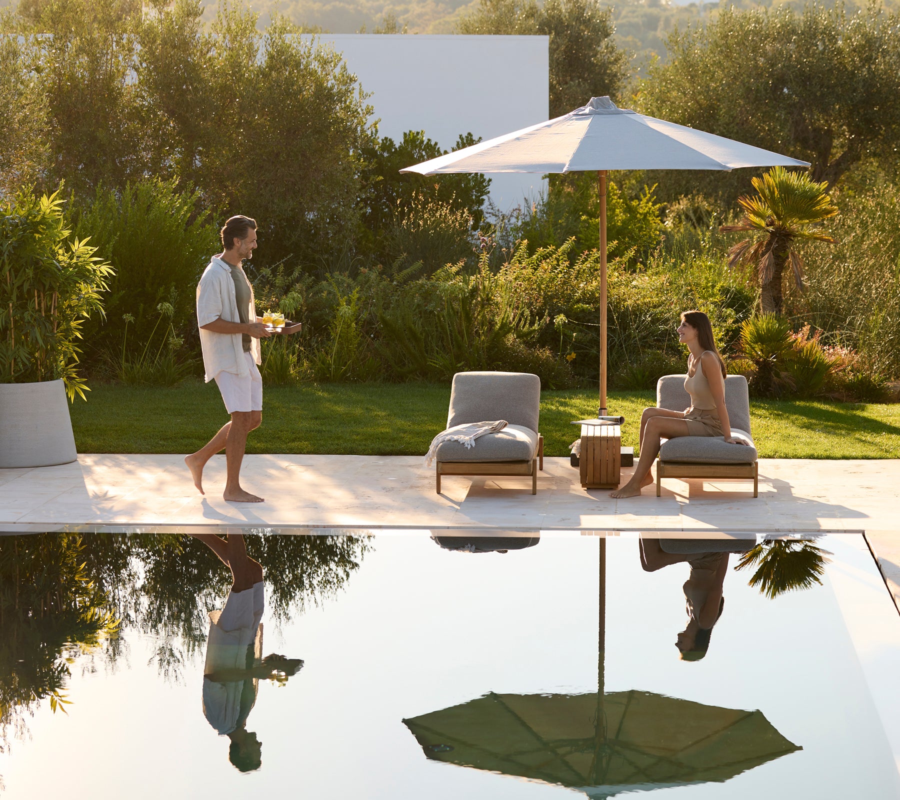 Moderne Lounge-Bereich im Freien mit grauen Stühlen, einem Holztisch und einem grünen Sonnenschirm.