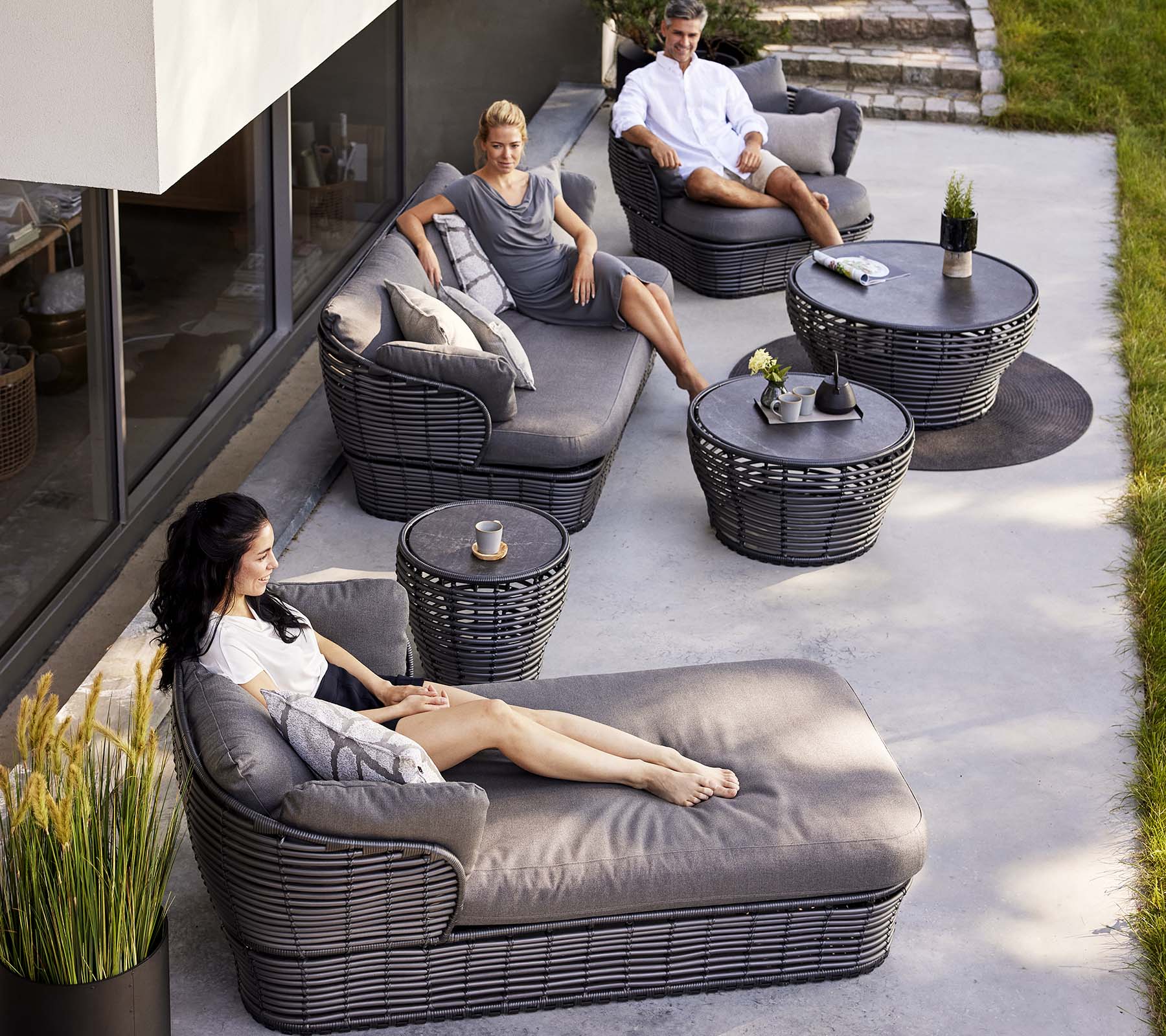 Moderne Lounge-Bereich mit einem Korb-Tagbett, einem 3-Sitzer-Sofa und Lounge-Stühlen, ergänzt durch runde Tische und dekorative Pflanzen.
