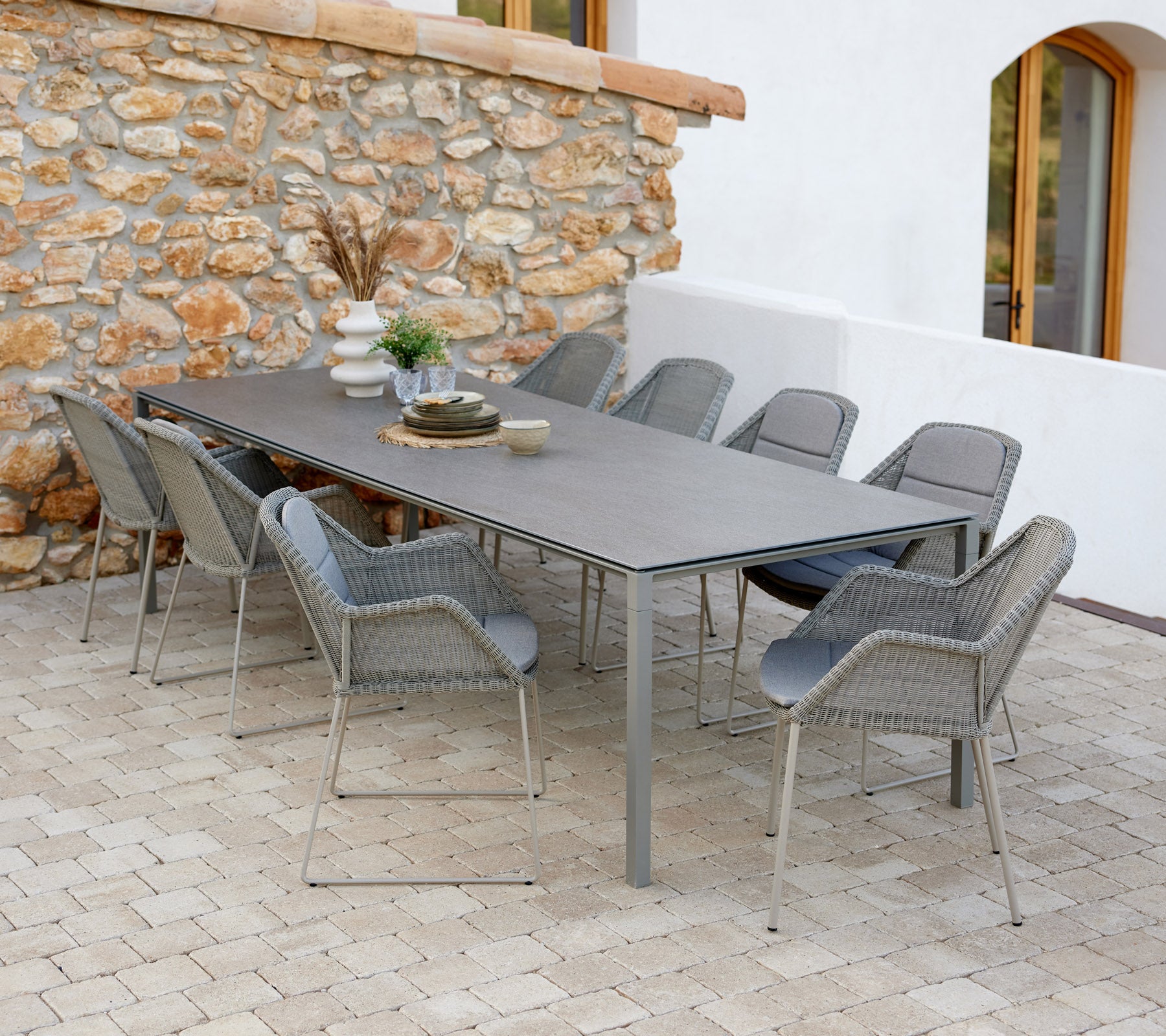 Modernem Esstisch mit taupe-farbenen Stühlen, dekoriert mit Gegenständen und einem Hauch von Grün vor einer Steinwand.