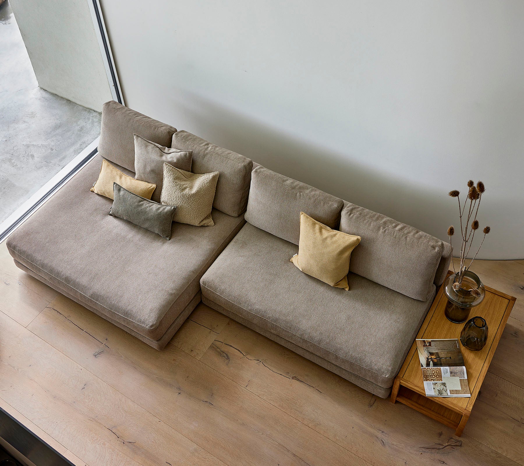 Ein stilvolles Sofa in neutralem Farbton, geschmückt mit verschiedenen dekorativen Kissen, begleitet von einem Holztisch mit Büchern und einer Vase.