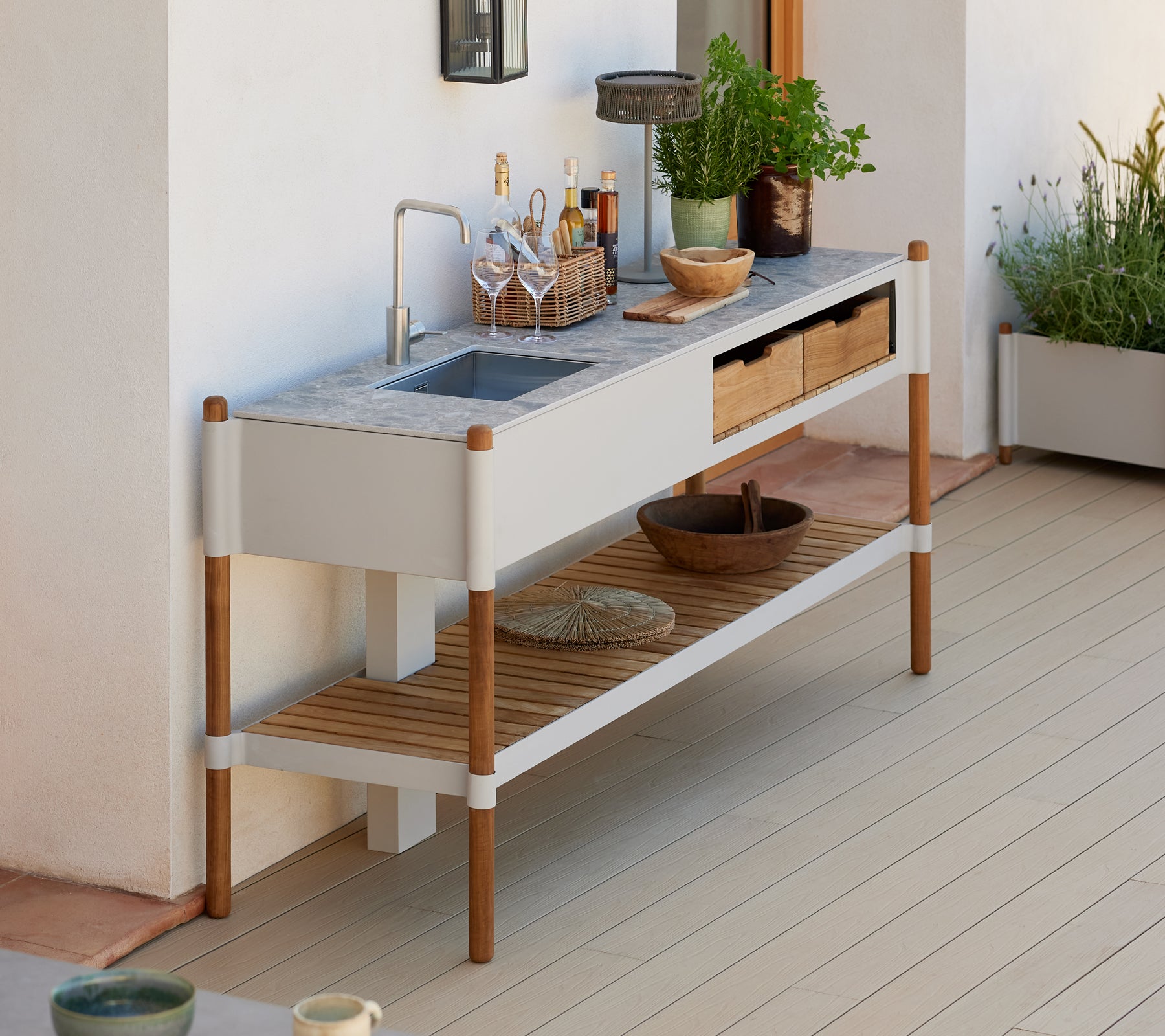 Ein modernes, minimalistisches Außenspülbecken mit einer Arbeitsplatte aus Granit, Holzaufbewahrungsschubladen und dekorativen Pflanzenarrangements.