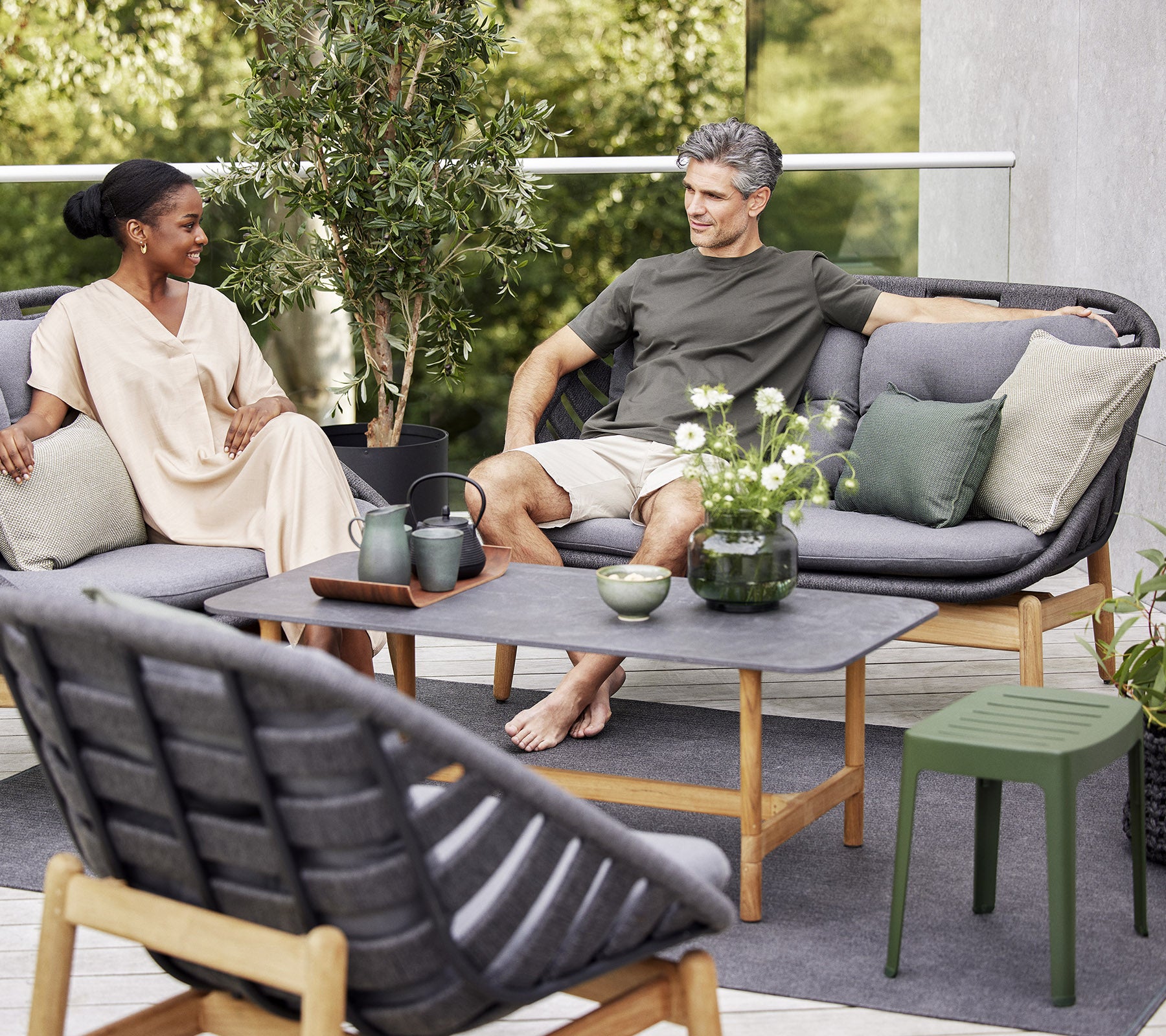 Zwei Personen entspannen sich auf einer stylischen Außensofa, umgeben von Grün und dekorativen Pflanzen, und genießen einen friedlichen Moment zusammen.